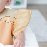 Close-up of a child in a high chair wearing a Bumkins Ruffle Apron Bib: Belle, with focus on the ruffle sleeve.