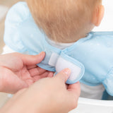 Adult hands fasten the hook-and-loop closure of a Bumkins Ruffle Apron Bib: Cinderella around a child's neck.