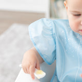 Close-up of a baby in a Bumkins Ruffle Apron Bib: Cinderella holding a spoon, with focus on the ruffle sleeve.
