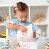 A girl sits at a table in a playroom with Bumkins Snack In Character 4-Piece Set: Disney Princess Magic Cinderella.