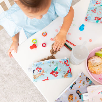 Aerial view of a girl with crafts and snacks at a white table with Bumkins Snack In Character 4-Piece Set: Disney Princess Magic Cinderella.