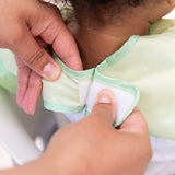 Adult hands fasten the hook-and-loop closure of a Bumkins Ruffle Apron Bib: Tiana around a child's neck.