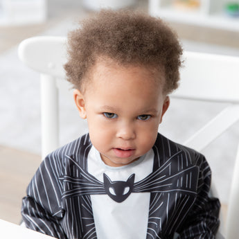 Close-up of a curly-haired boy wearing a bib from Bumkins Snack In Character 3-Piece Set: Disney Everyday Is Halloween Jack.