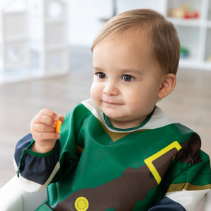 A child in a bib from Bumkins Snack In Character 4-Piece Set: Nintendo Zelda holds an orange cracker.