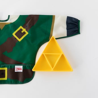 Bumkins Sleeved Bib: Zelda™ lays flat next to a yellow triangle-shaped divided plate on a white background.