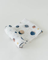 The Little Unicorn Cotton Swaddle, Planetary features hand-painted space-themed prints of planets and stars on light gray cotton muslin.