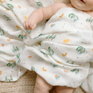 A baby lies on a woven surface, wrapped in LouLou Lollipops Eric Carle World of Wonder muslin swaddle with OEKO-TEX Standard 100.