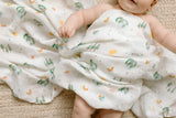 A baby lies on a woven surface, wrapped in LouLou Lollipops Eric Carle World of Wonder muslin swaddle with OEKO-TEX Standard 100.