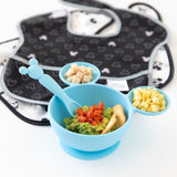 Bumkins Silicone First Feeding Set: Mickey Mouse Light Blue, with mashed avocado and corn, sits next to stacked bibs on a white background.