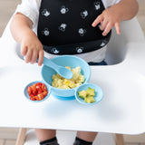 A toddler in a high chair eats scrambled eggs, tomatoes, and avocado from a Bumkins Silicone First Feeding Set: Mickey Mouse Light Blue.