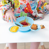 A child enjoys applesauce, raspberries, and a muffin from the Bumkins Silicone First Feeding Set: Mickey Mouse Light Blue on a highchair.