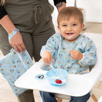 A mom and baby use Bumkins On-The-Go Mealtime 5-Piece Set: Mickey + Minnie Mouse Sunny Side Up Blue at meal time in a bright room.