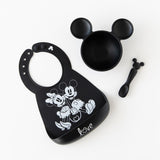 Bumkins Silicone First Feeding Set: Mickey Mouse Classic Black sits on a white background near a silicone bib with Mickey & Minnie design.