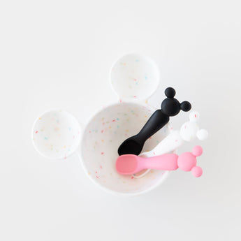 Bumkins Silicone First Feeding Set: Mickey Mouse Vanilla Sprinkle sits on a white background with black and pink baby spoons.