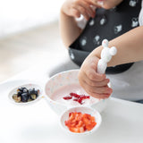 A child in a high chair enjoys yogurt with berries using a Bumkins Silicone First Feeding Set: Mickey Mouse Vanilla Sprinkle.