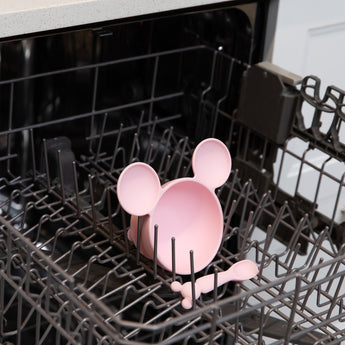 A bowl & spoon from Bumkins On-The-Go Mealtime 5-Piece Set: Mickey + Minnie Mouse Sunny Side Up Pink sit in the top rack of a dishwasher.