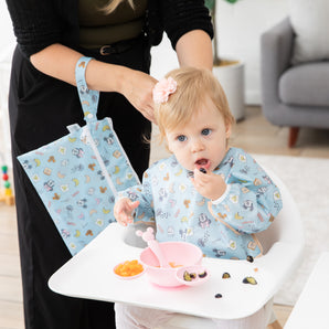 A mom and baby use Bumkins On-The-Go Mealtime 5-Piece Set: Mickey + Minnie Mouse Sunny Side Up Pink at meal time in a cozy living room.