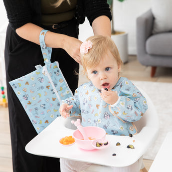 A mom and baby use Bumkins On-The-Go Mealtime 5-Piece Set: Mickey + Minnie Mouse Sunny Side Up Pink at meal time in a cozy living room.