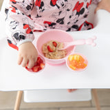 A child enjoys oatmeal with fruit from Bumkins Silicone First Feeding Set: Minnie Mouse Light Pink on their high chair tray.