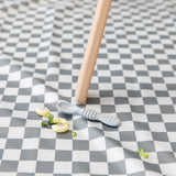 A Bumkins Silicone Dipping Spoons 3 Pack: Taffy lays atop a gray & white checkered mat among pieces of pasta & broccoli by a high chair leg.