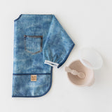 Bumkins Silicone First Feeding Set: Sand rests next to a folded denim print sleeved bib on a white background.