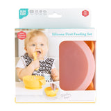 Baby using a spoon with a yellow bowl. Silicone First Feeding Set: Tangerine by Bumkins features a pink bowl with a suction base.