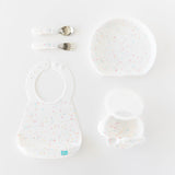 Bumkins Silicone First Feeding Set: Vanilla Sprinkle sits among a matching bib, plate, and utensils on a white background.