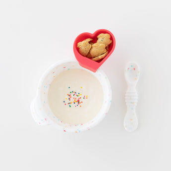 Bumkins Silicone First Feeding Set: Vanilla Sprinkle filled with yogurt & sprinkles, and a heart-shaped cup of cookies on a white background.