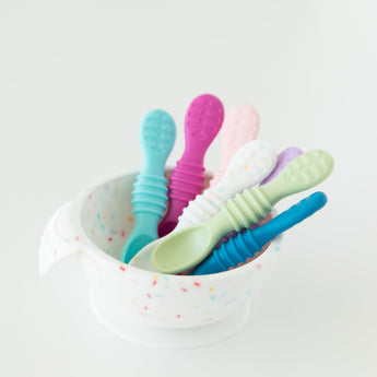 Bumkins Silicone First Feeding Set: Vanilla Sprinkle with colorful baby spoons inside on a white background.