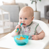 A baby enjoys mashed sweet potatoes with a bowl & spoon from Bumkins First Foods Essential 5-Piece Mealtime Set: Blue Jelly.