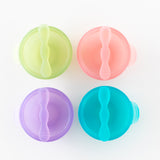 Top down view of 4 colorful bowls with spoons, including Bumkins Silicone First Feeding Set: Pink Jelly, neatly arranged on a white background.