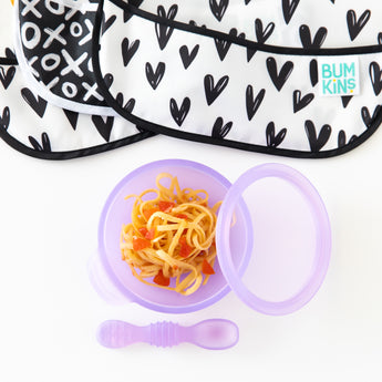 Bumkins Silicone First Feeding Set: Purple Jelly with spaghetti on a white background, with black and white bibs nearby.