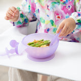 A child enjoys mealtime with Bumkins Silicone First Feeding Set: Purple Jelly, wearing a colorful bib in a high chair.
