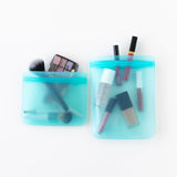 Bumkins Silicone Flat Reusable Bag 2 Pack, Blue holds makeup essentials on a white background—brushes, lipsticks, and an eyeshadow palette.