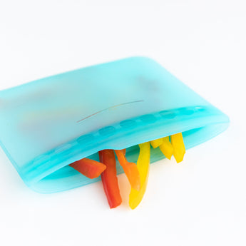 A Bumkins Silicone Flat Reusable Bag 2 Pack, Blue packed with colorful bell pepper slices on a white background.