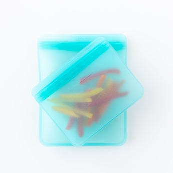 Bumkins Silicone Flat Reusable Bag 2 Pack, Blue rests on a white background, filled with bell pepper slices.