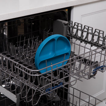 Open dishwasher with Bumkins Silicone Grip Dish: Dark Blue, ideal for toddler portions, neatly placed on the rack.
