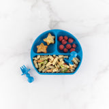 Bumkins Silicone Chewtensils®: Dark Blue and a blue divided plate with pasta, berries, & potatoes rest on a marble background.