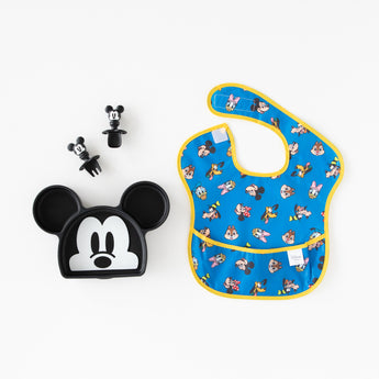 Bumkins Grip Dish Essential Infant 3-Piece Mealtime Set: Disney Mickey Mouse lays next to a blue patterned bib on a white background.