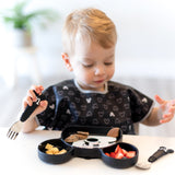 A toddler joyfully self-feeding from the Bumkins Essential Mealtime Set, Mickey Mouse, eating pancakes and fruit.
