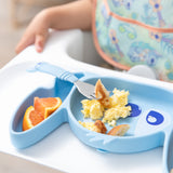 Close-up of a child in a high chair with a Bumkins Silicone Grip Dish: Stitch filled with eggs, pancakes, and orange slices; a fork on top.