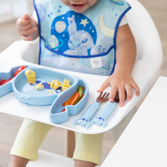 Close-up of a child in a high chair reaching for Bumkins Grip Dish Essential 3-Piece Mealtime Set: Disney Stitch.