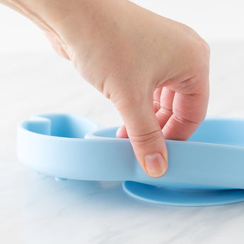 A hand holds a dish from Bumkins Grip Dish Essential 3-Piece Mealtime Set: Disney Stitch, demonstrating the suction cup bottom.