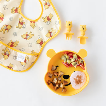 Bumkins Grip Dish Essential Infant 3-Piece Mealtime Set: Disney Winnie the Pooh holds yogurt & fruit next to a bib on a white background.