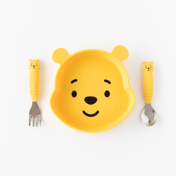 Bumkins Spoon + Fork: Winnie the Pooh rests next to a Winnie the Pooh-shaped plate on a white background.