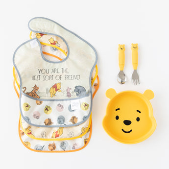 Bumkins Spoon + Fork: Winnie the Pooh lays next to 3 waterproof bibs and a Winnie the Pooh-shaped plate on a white background.