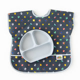 A gray divided plate sits on top of a Bumkins Junior Bib: Super Mario™ Lineup on a white background.