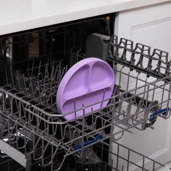 A Lavender Bumkins Silicone Grip Dish with divided sections sits in an open dishwasher.
