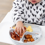 Close-up of a child in a black & white bib reaching for breakfast foods from a Bumkins Silicone Grip Dish: Marble on a high chair tray.