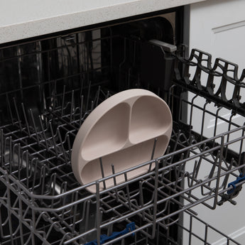 A dish from Bumkins On-The-Go Mealtime 6-Piece Set: Wander + Sand sits in the top rack of an open dishwasher.